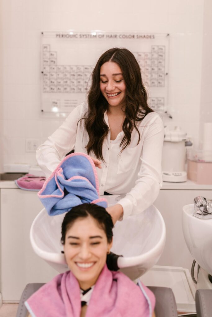 Two women smiling during a relaxing hair wash session in a modern salon.